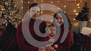 Portrait of happy young family sitting together on sofa In lounge at home on christmas day, smiling and looking at