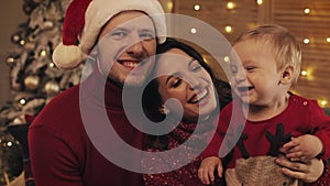 Portrait of happy young family sitting together on sofa In lounge at home on christmas day, smiling and looking at