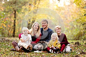 Portrait of Happy Young Family with three Cute, Smiling Children and their Pet Dog on Autumn Day