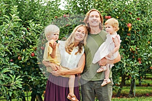Portrait of happy young family with two little children enjoying good time in apple orchard