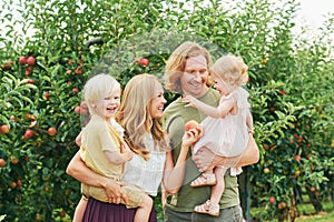 Portrait of happy young family with two little children enjoying good time in apple orchard