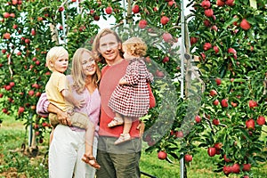 Portrait of happy young family with two little children enjoying good time in apple orchard