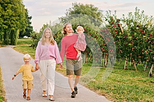 Portrait of happy young family with two little children enjoying good time in apple orchard