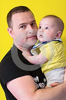 Portrait of happy young father holding baby isolated on yellow