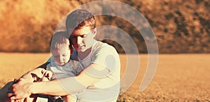 Portrait of happy young father and son child together sitting on grass in sunny evening park