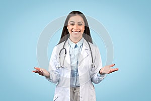 Portrait of happy young female doctor in white coat with stethoscope on neck gesturing, talking and smiling at camera