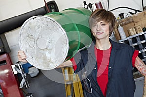 Portrait of a happy young female mechanic carrying oil drum on shoulder in car workshop