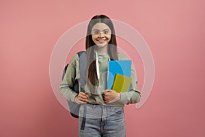 Portrait of happy young female student with backpack and books posing over pink studio background