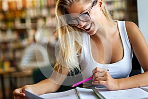 Portrait of happy young female student taking notes from a book at college library.