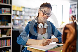 Portrait of happy young female student taking notes from a book at college library.