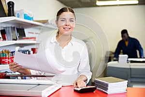 Portrait of happy young female typographer using paper cutter cutter during work in the printer shop