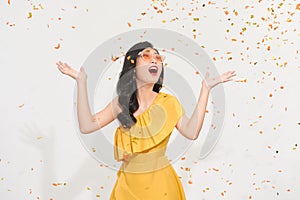 Portrait of a happy young girl in summer clothes standing under confetti rain isolated over white background