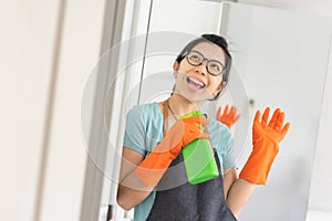 Portrait Happy Young girl wear eyeglasses holding green cleaner spray bottle like at microphone singing in white room. Smiling