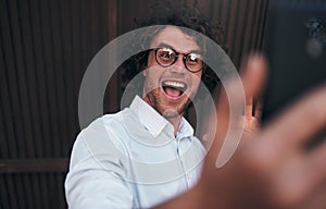 Portrait of happy young handsome businessman taking self portrait with his smart phone outdoors. Happy smiling male wearing white