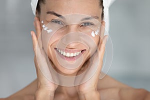 Portrait of happy young hispanic woman applying cream.