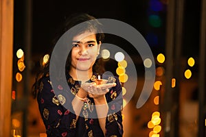 Portrait of Happy Young indian beautiful woman holding diya/clay oil lamps wearing traditional dress,celebrates diwali,at home,