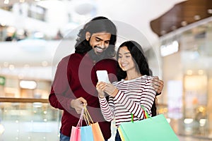 Portrait of happy young indian couple using smartphone while shopping