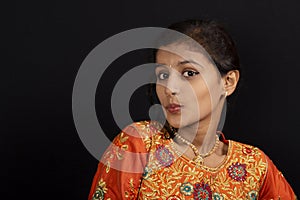 Portrait of a happy young Indian girl pursing her lips on black background.