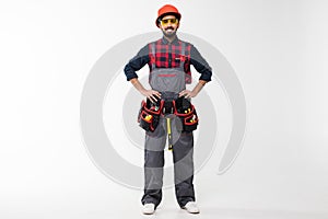 Portrait of happy young indian male construction worker with tool belt isolated on white background