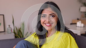 Portrait of happy young indian woman smile at camera sitting on sofa at home