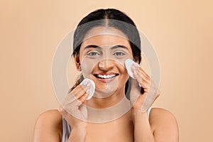 Portrait of happy young indian woman using cotton pads on her face