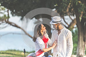 Portrait of happy young love couple on scooter enjoying themselves in a park at summer time