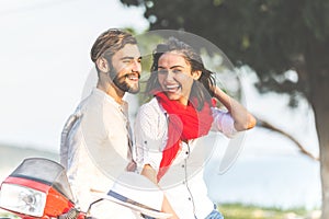 Portrait of happy young love couple on scooter enjoying themselves in a park at summer time