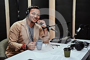 Portrait of happy young male radio host having a drink, smiling at camera while moderating a live show
