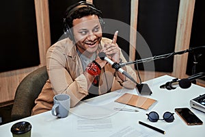 Portrait of happy young male radio host smiling while talking, broadcasting in studio using microphone and headphones