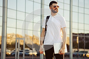 Portrait of a happy young man in casual clothes, with a laptop in his hands. Successful business man on city street