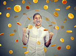 Portrait of a happy young man celebrating financial success under a bitcoin rain
