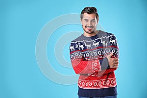 Portrait of happy young man in Christmas sweater on light blue background