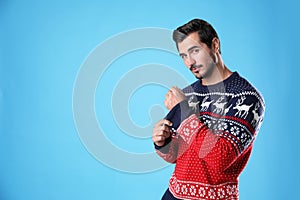 Portrait of happy young man in Christmas sweater on light blue background.