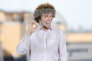 Portrait of a happy young man with curly hair shows okay gesture sign.