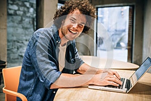 Portrait of happy young man with curly hair using laptop for working and browsing online. Smart Caucasian male reading news,