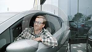 Portrait of a happy young man driving a new luxury electric car in a car dealership