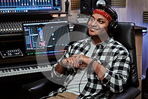 Portrait of happy young man, male artist in headphones smiling aside while sitting in recording studio