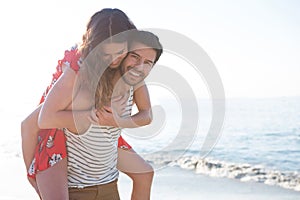 Portrait of happy young man piggybacking his girlfriend at beach