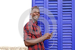 Happy young man standing outdoors listening music with mobile phone