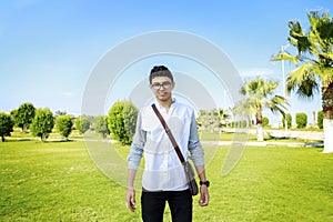 Portrait of a happy young man standing outdoors with small bag.