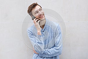 Happy young man talking with mobile phone by wall