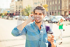 Portrait of happy young man talking on phone and walking on the street