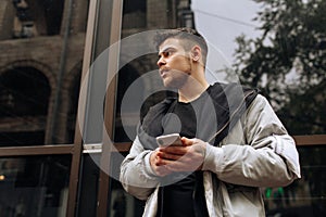 Portrait of happy young man walking on the street and looking aside while talking by his phone