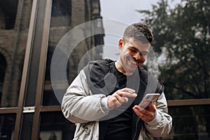 Portrait of happy young man walking on the street and looking aside while talking by his phone