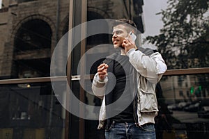 Portrait of happy young man walking on the street and looking aside while talking by his phone