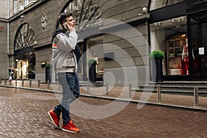 Portrait of happy young man walking on the street and looking aside while talking by his phone