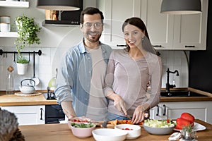 Portrait of happy young married couple cooking together in kitchen.