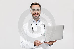 Portrait of happy young medical doctor with stethoscope working in clinic and holding laptop