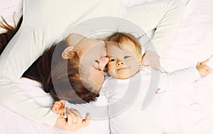 Portrait of happy young mother and cute baby lying on the bed at home together