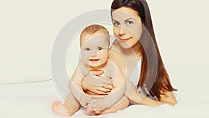 Portrait of happy young mother and cute baby lying on the bed at home together on white background